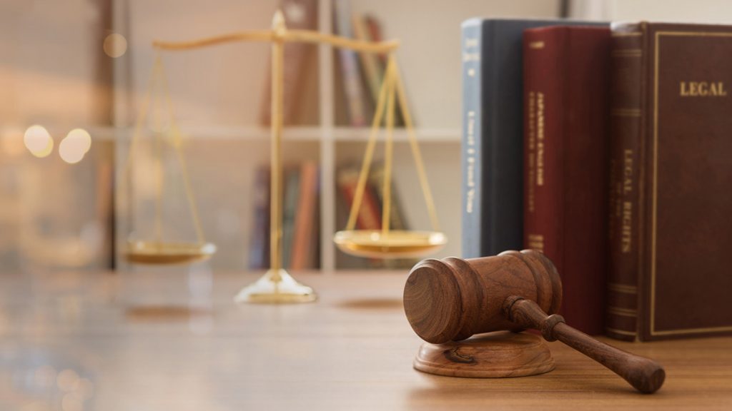 A gavel on a desk in front of the scales of justice and legal books