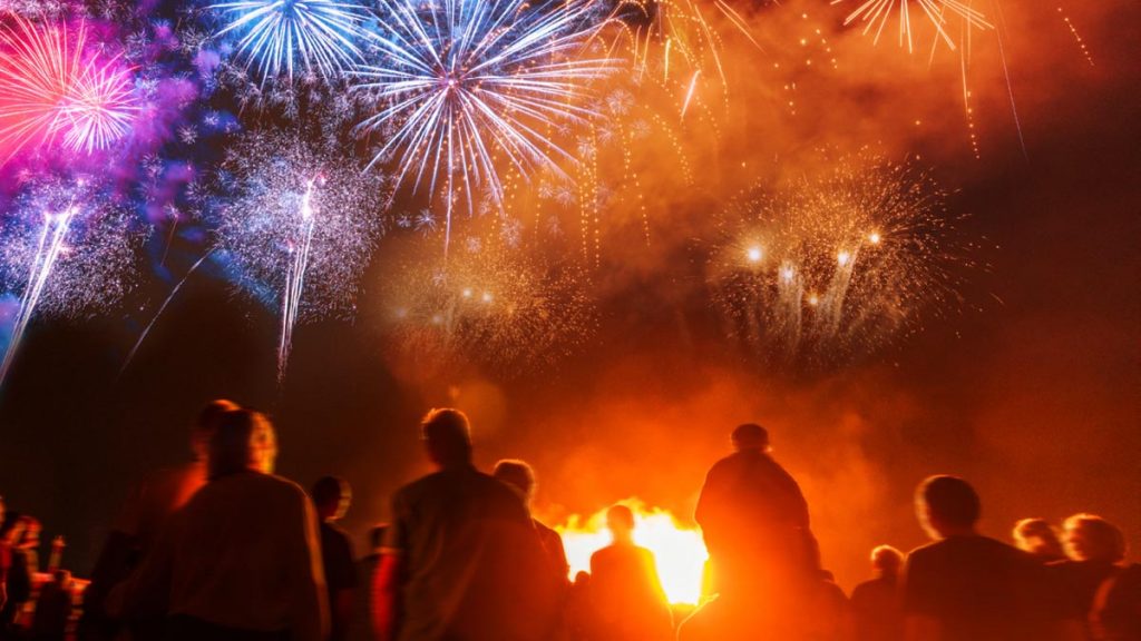 Crowd of people with necks craned to watch fireworks in the sky at night