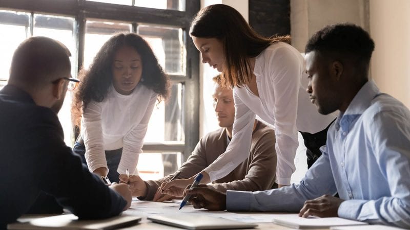 Focused diverse team people discuss corporate paperwork share ideas