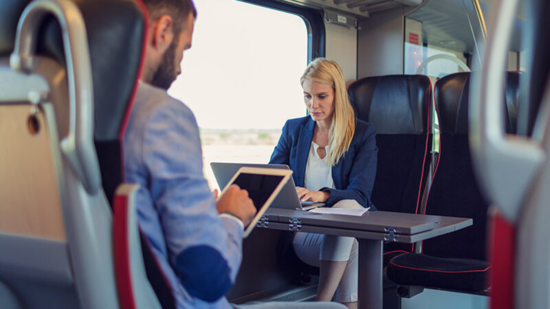 Two people working while seated on a train.